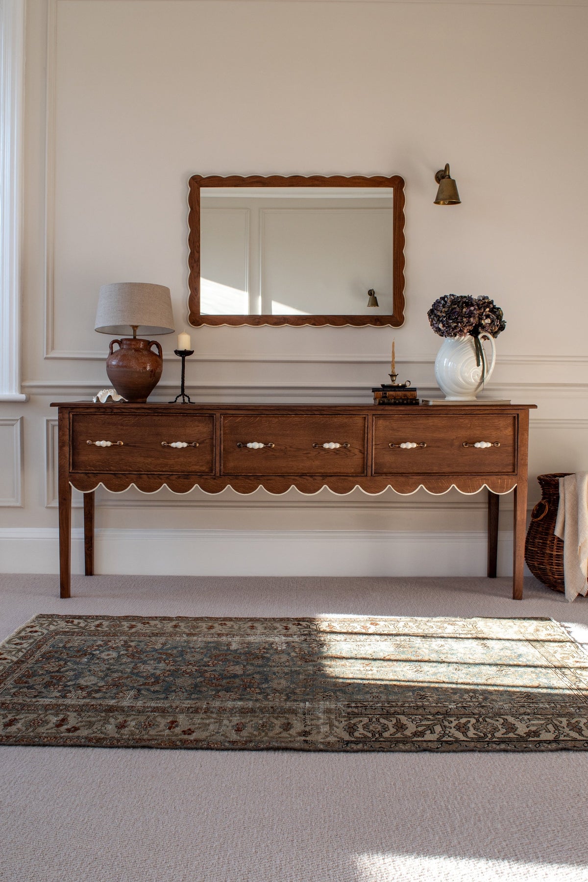 Photograph of a sideboard in a living room with rug, mirror and decorative vase and lamp