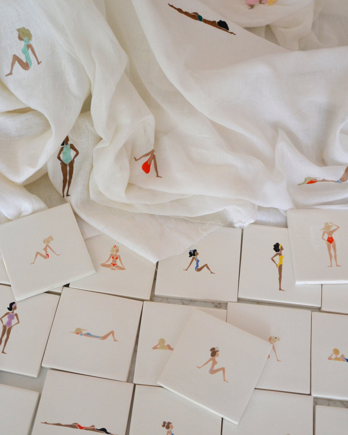Hand painted coasters and embroidered napkins with figures of women sunbathing