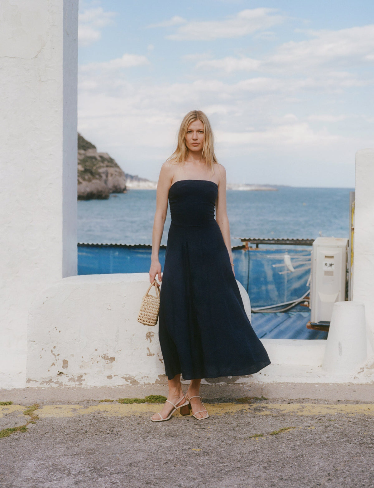 Woman in a strapless dress standing on a street with the ocean in the background