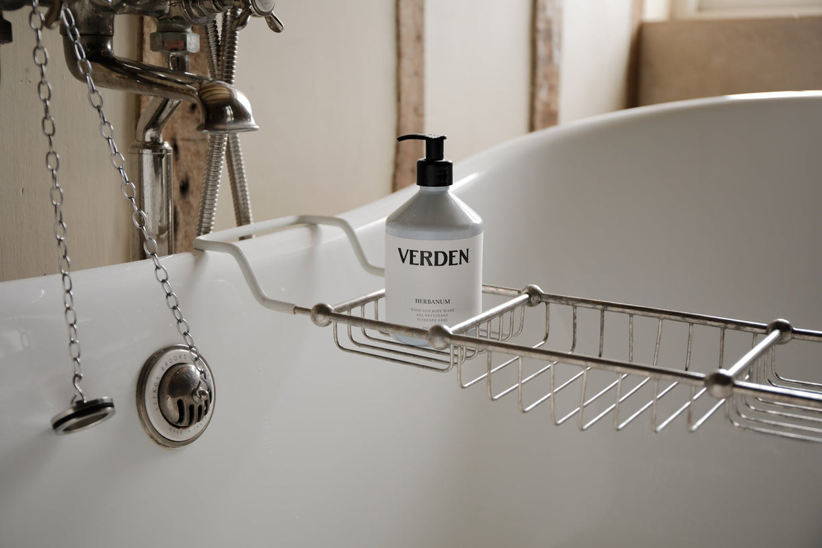 Close up image of a bath tub with silver tray with a blue bottle with the label Verden