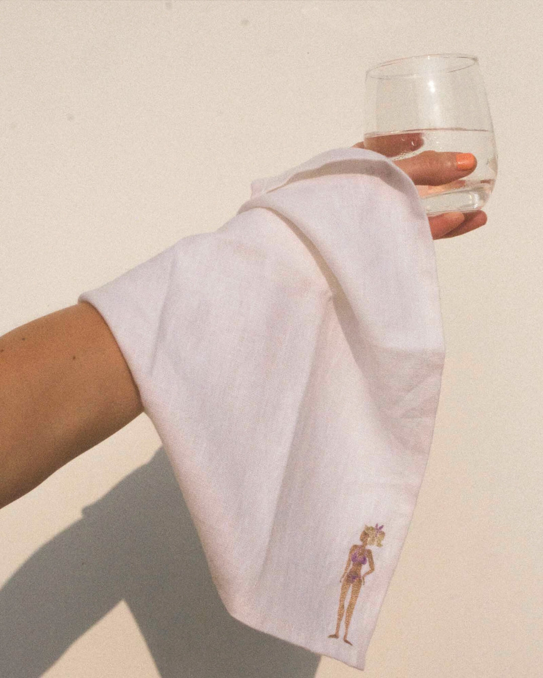 Hand holding a glass of wine with a decorative napkin featuring a bikini-clad figure.