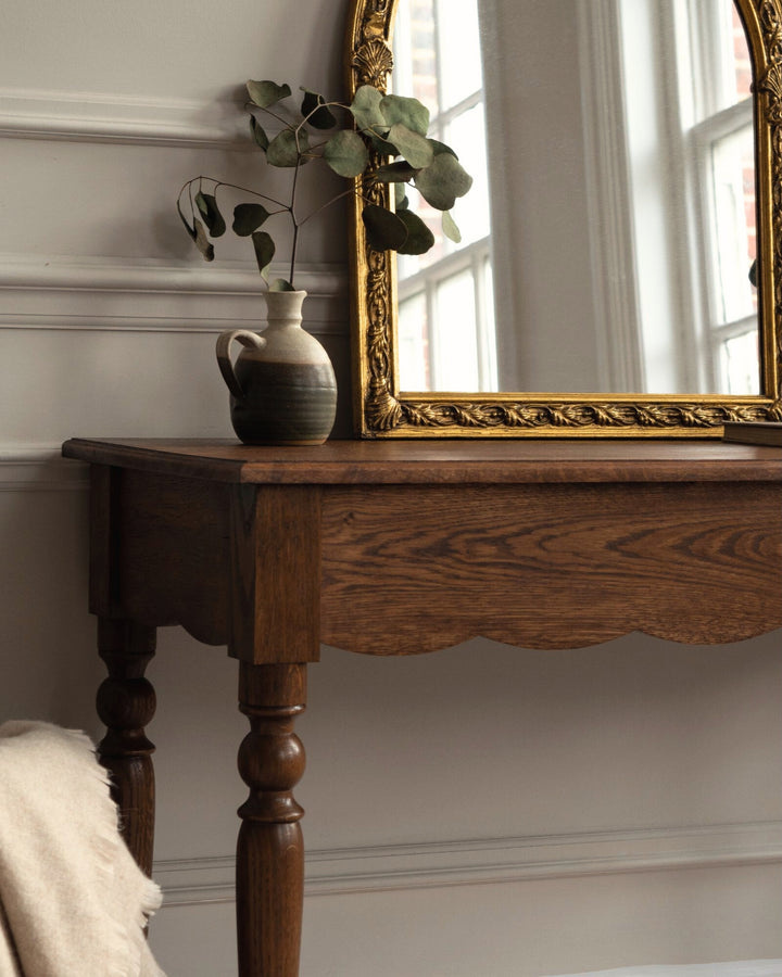 Wooden table with a vase and decorative mirror in a room with large windows.