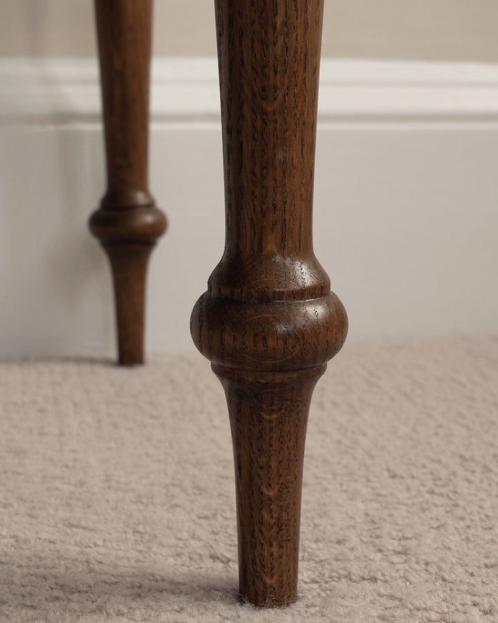 Close-up of a wooden leg on a carpeted floor with a neutral wall background
