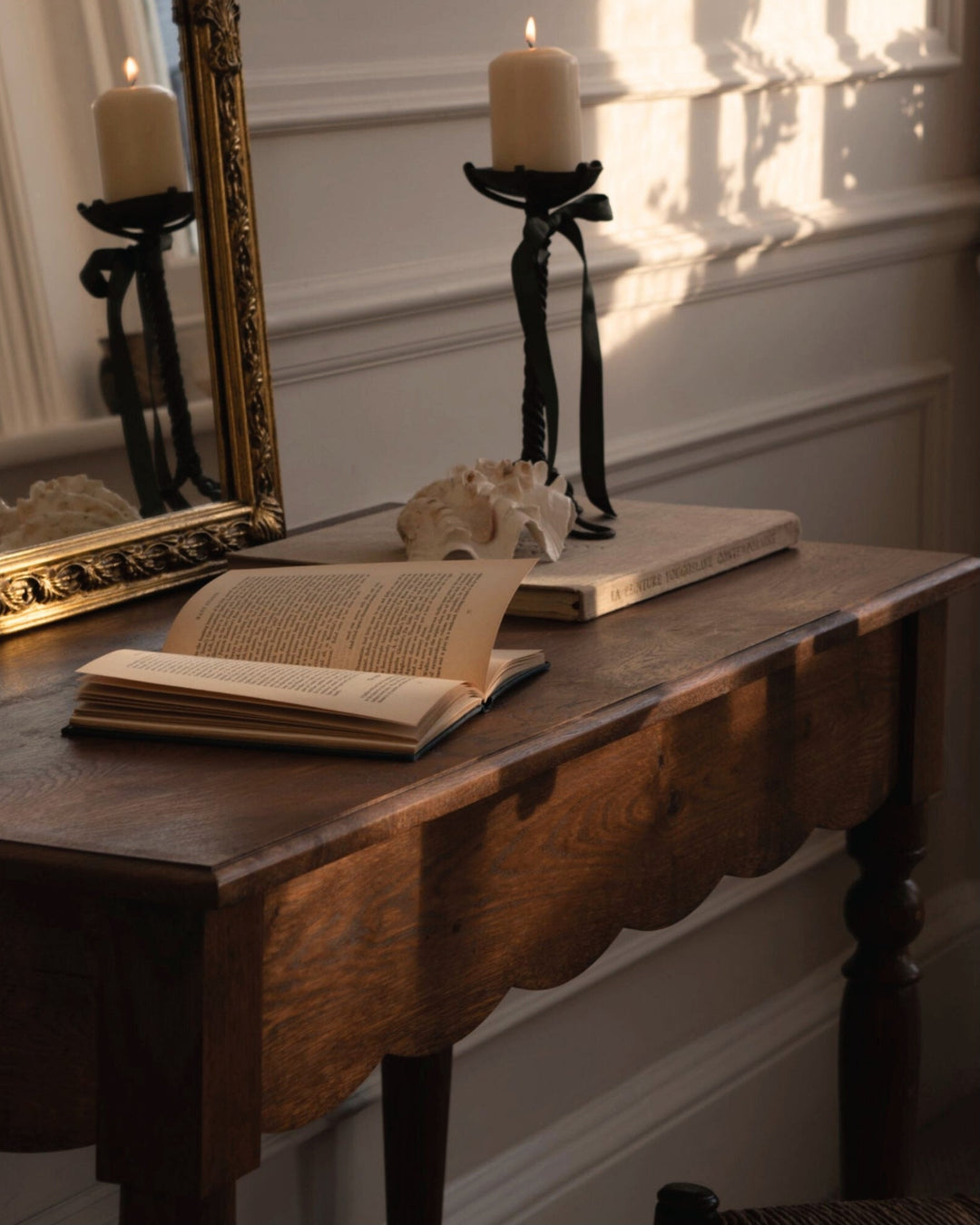 Wooden table with books and candles in a room with sunlight streaming in