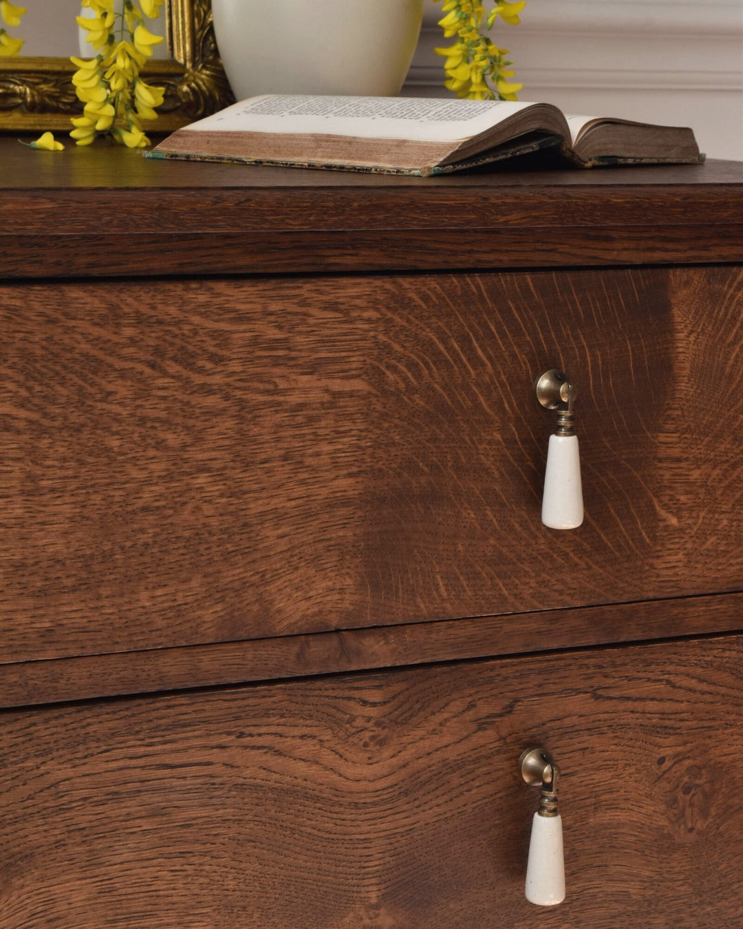 Wooden chest with white handles on a wooden surface with an open book and yellow flowers.