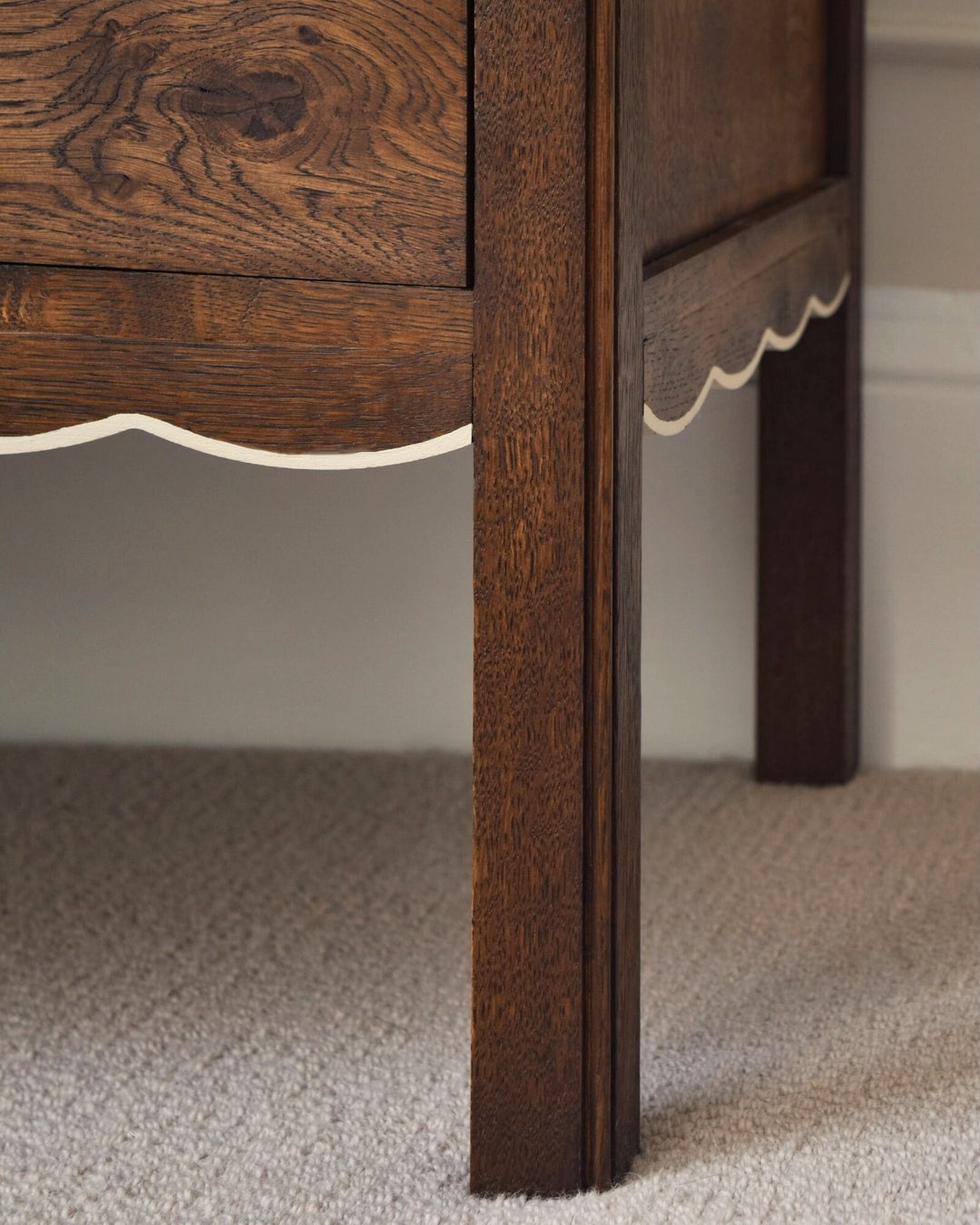 Close-up of a wooden furniture leg with a scalloped edge on a carpeted floor.