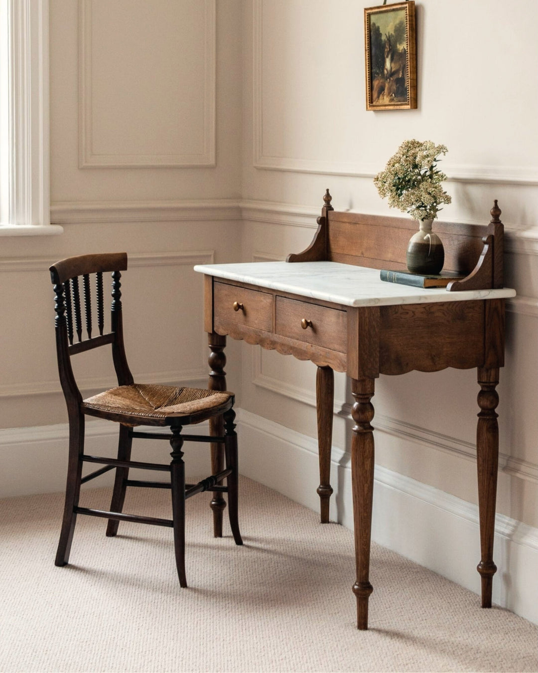 Wooden desk with marble top and chair in a room with a painting on the wall.