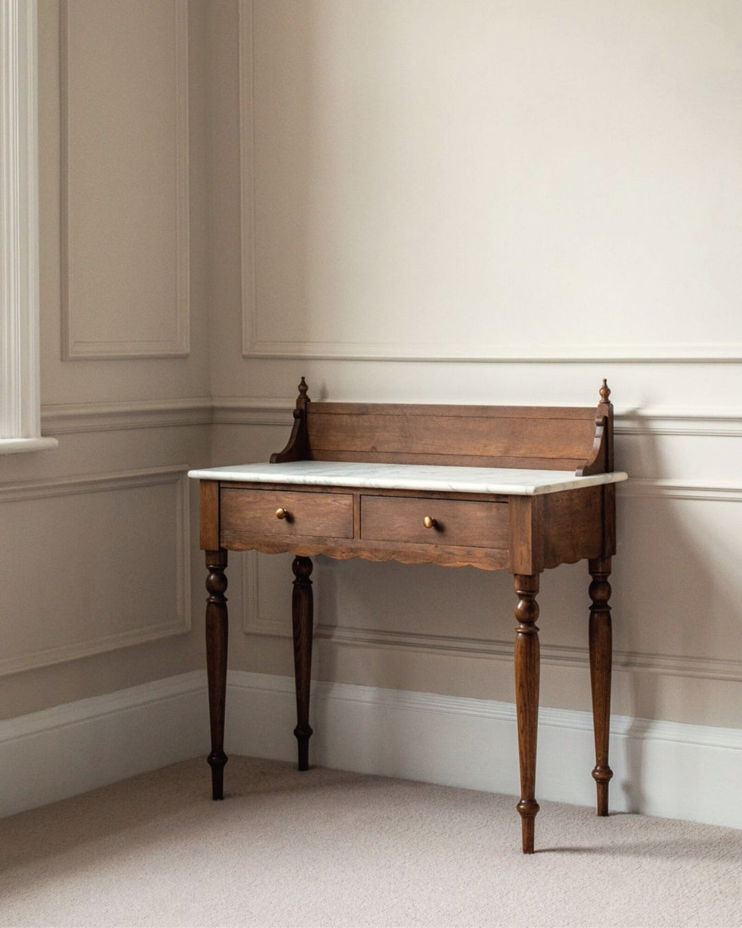 Wooden desk with marble top in a room with beige walls and carpet.