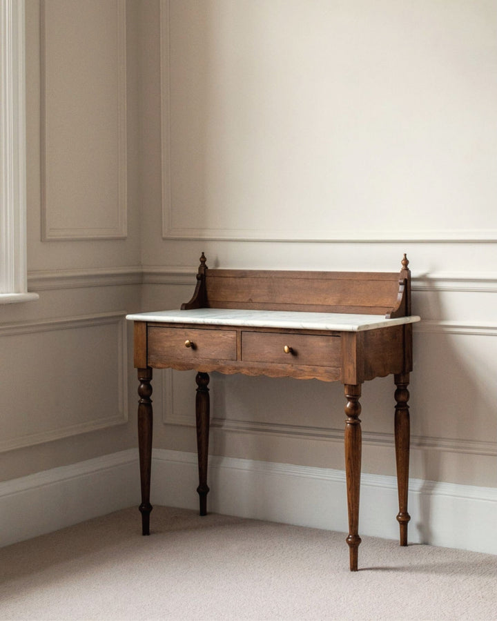 Wooden desk with marble top in a room with beige walls and carpet.