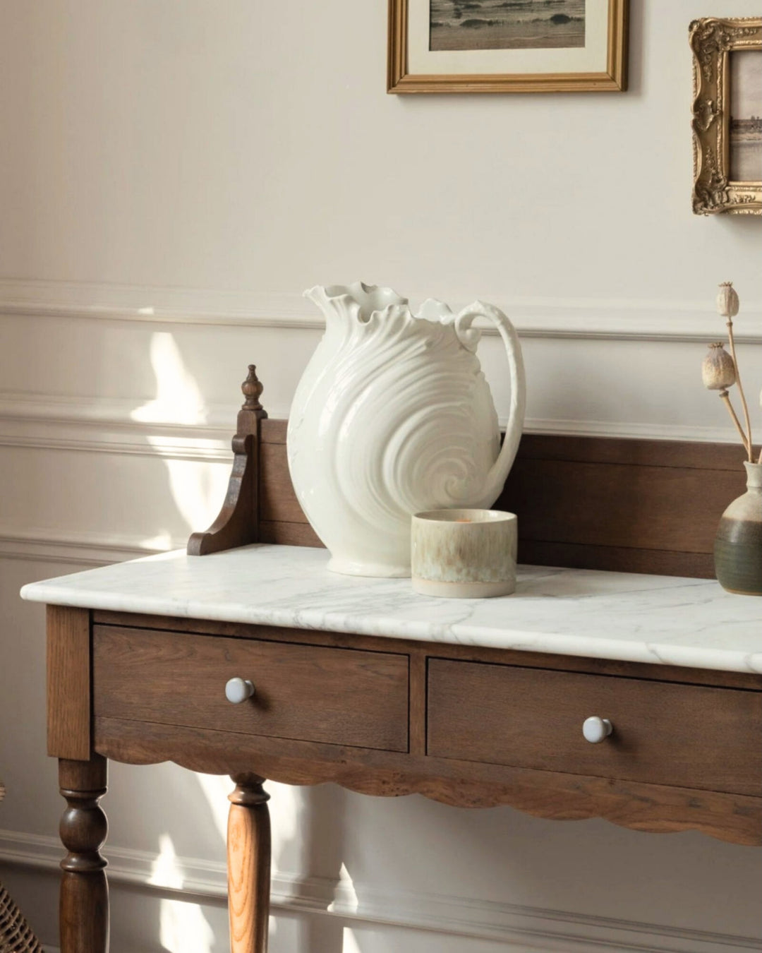 Wooden console table with marble top and decorative items against a wall with framed pictures.