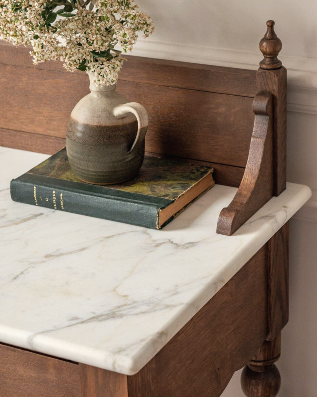Wooden desk with marble top, book, and ceramic pitcher on a neutral background