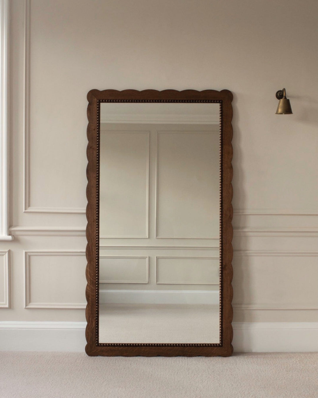 Wooden floor mirror with decorative frame on a beige wall.