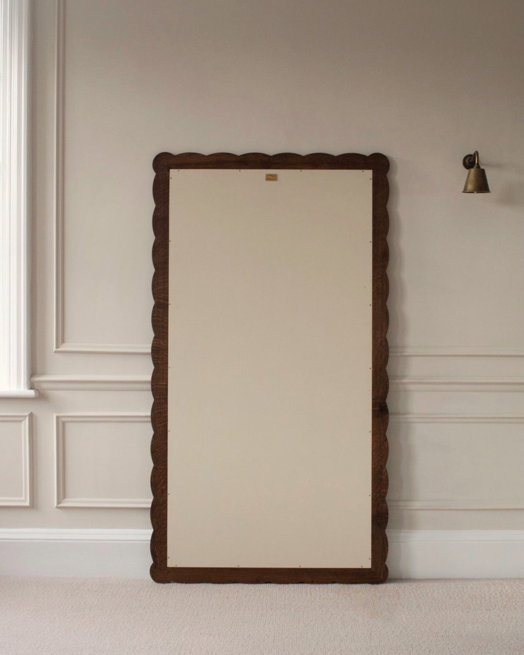 Large floor mirror with decorative wooden frame on a neutral wall.