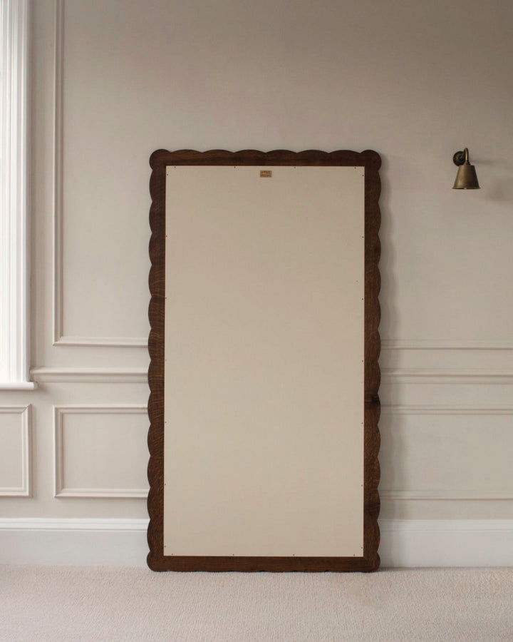 Large floor mirror with decorative wooden frame on a neutral wall.