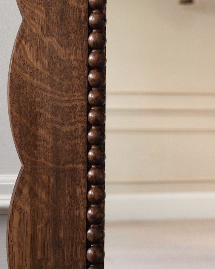 Close-up of a wooden mirror with bead detailing on a neutral background
