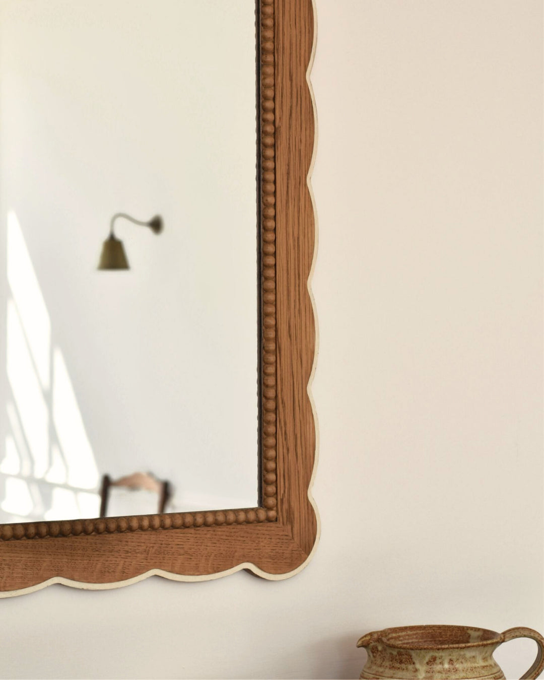 Wooden-framed mirror on a white wall with a decorative vase in the corner.