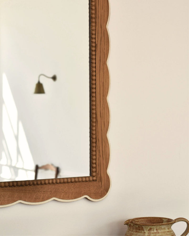 Wooden-framed mirror on a white wall with a decorative vase in the corner.
