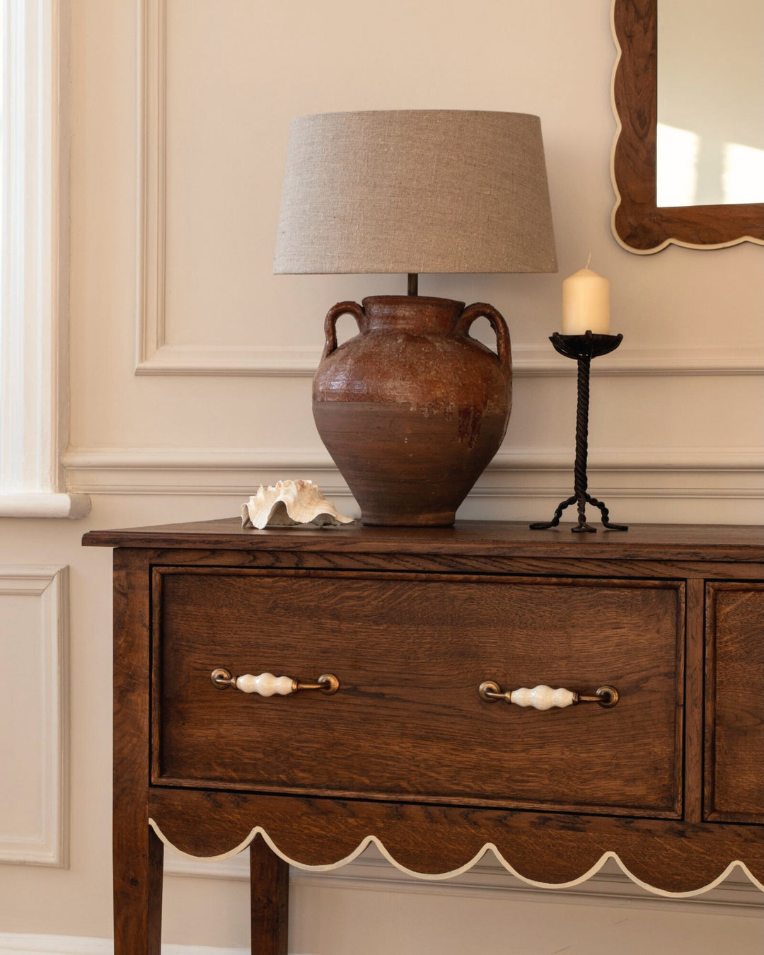 Wooden sideboard with a lamp, candle, and decorative items against a beige wall.