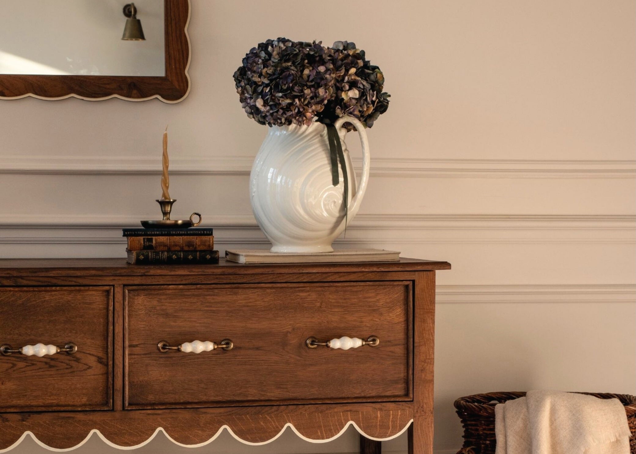Wooden sideboard with a vase of flowers and a basket in a room setting.