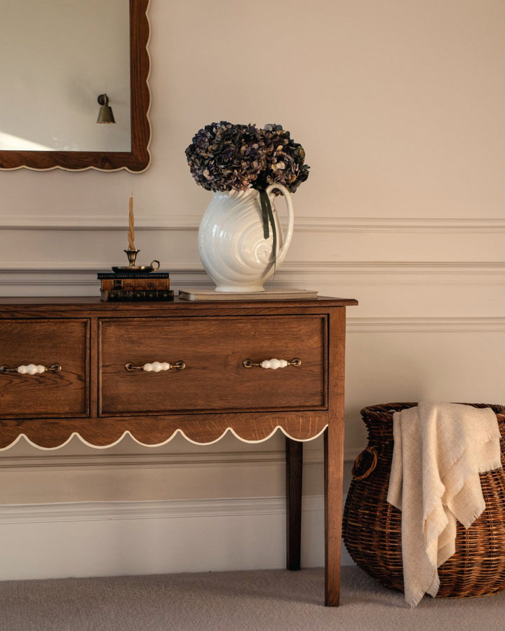 Wooden sideboard with a vase of flowers and a basket in a room setting.