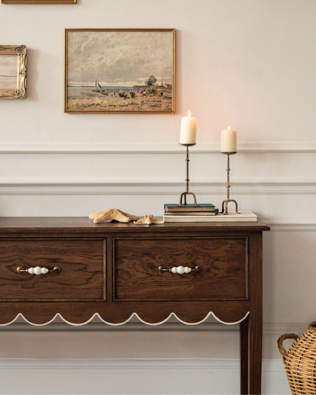 Wooden sideboard with candles and framed pictures on a wall.