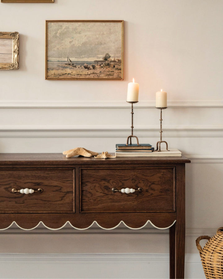 Wooden sideboard with candles and framed pictures on a wall.