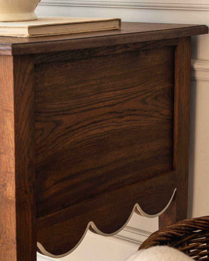 Wooden side table with a scalloped edge against a neutral wall.