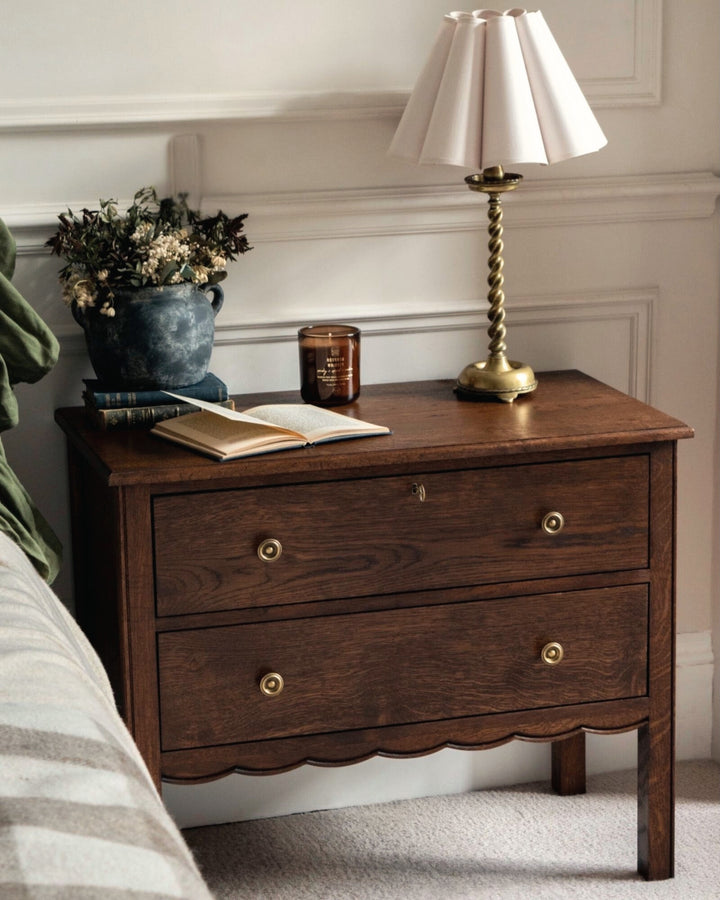 Wooden nightstand with a lamp, book, and candle in a bedroom setting.