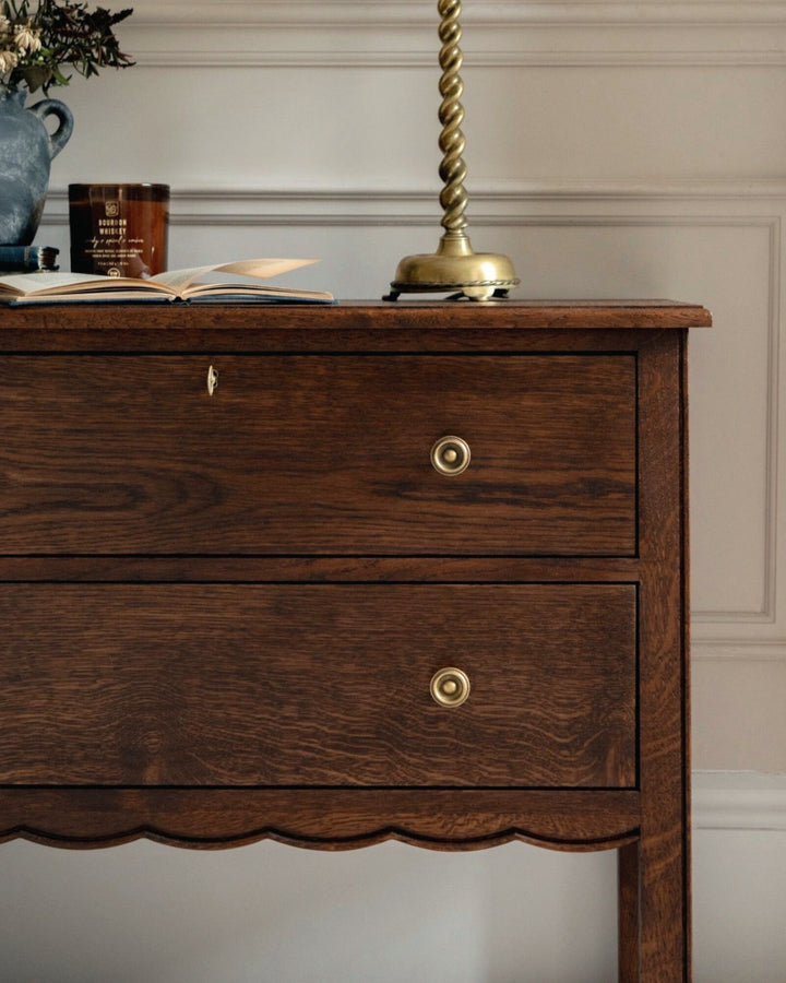 Wooden dresser with two drawers and gold knobs against a neutral wall.