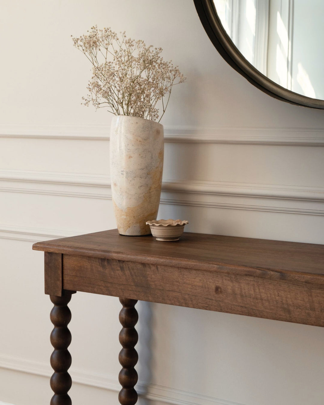 Wooden console table with a vase of dried flowers against a white wall.