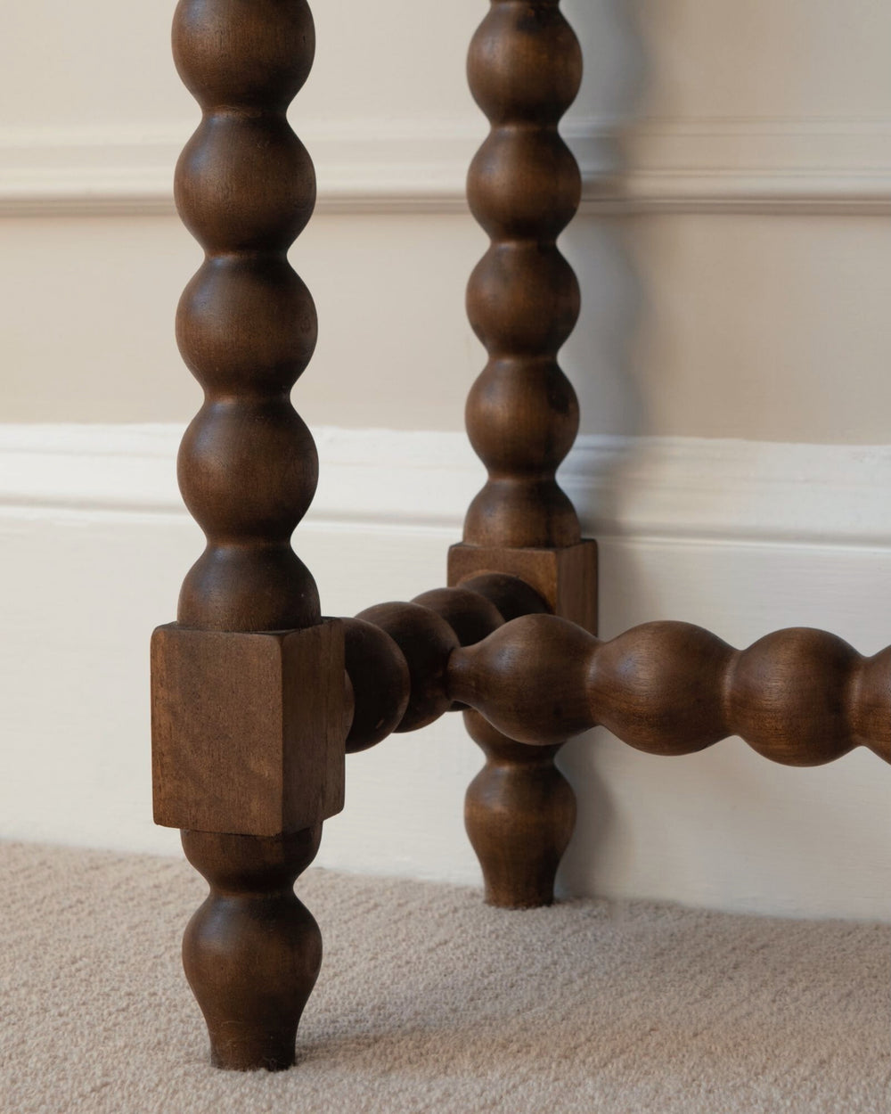 Close-up of a wooden spindle leg against a neutral wall.