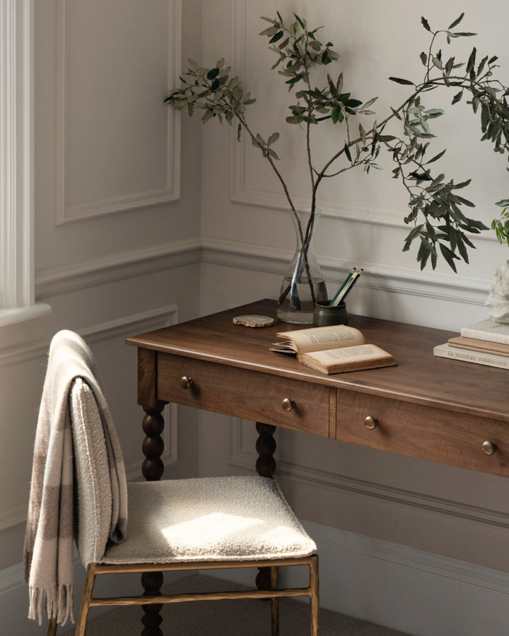 Wooden desk with chair and decorative elements in a room with white walls.