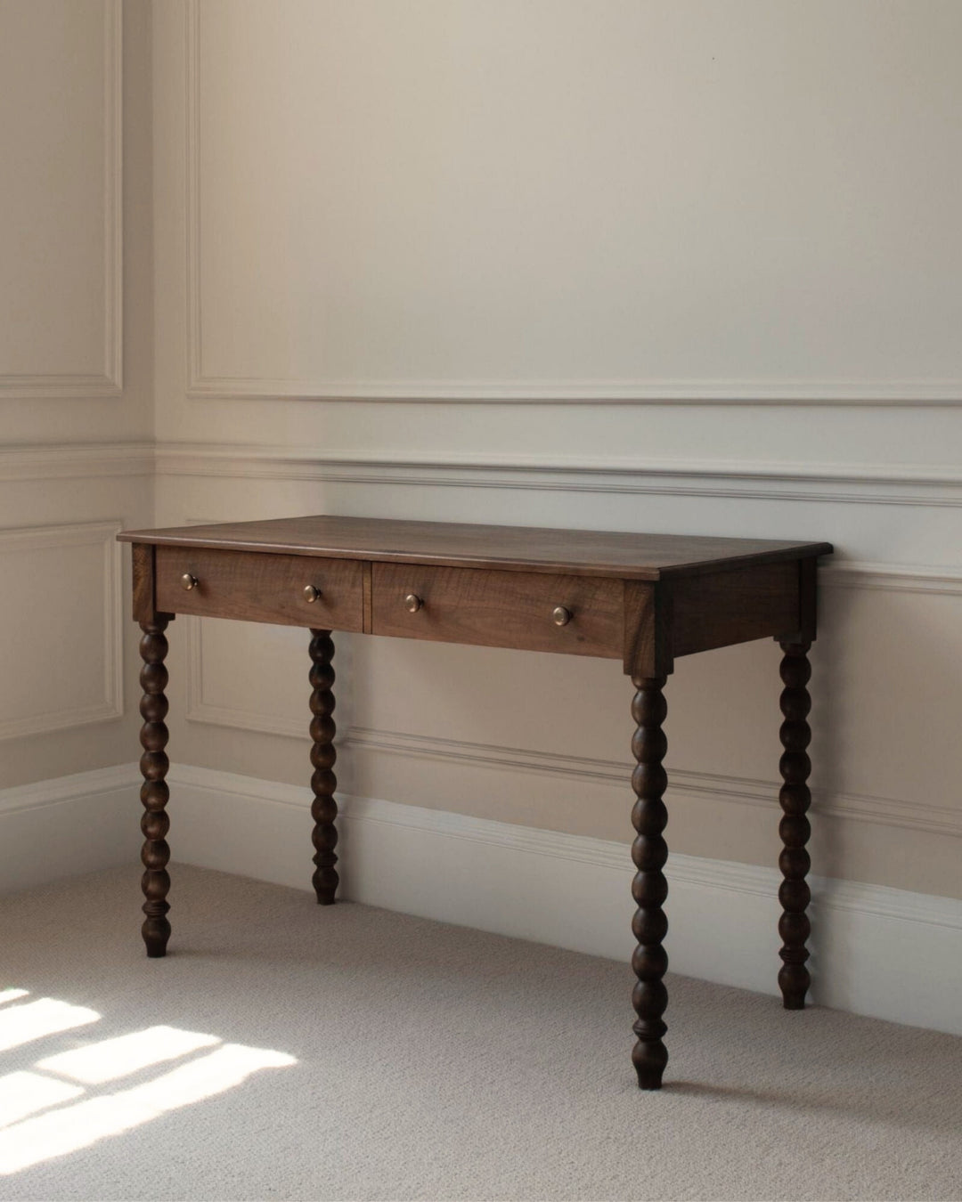 Wooden console table with spiral legs against a neutral wall.