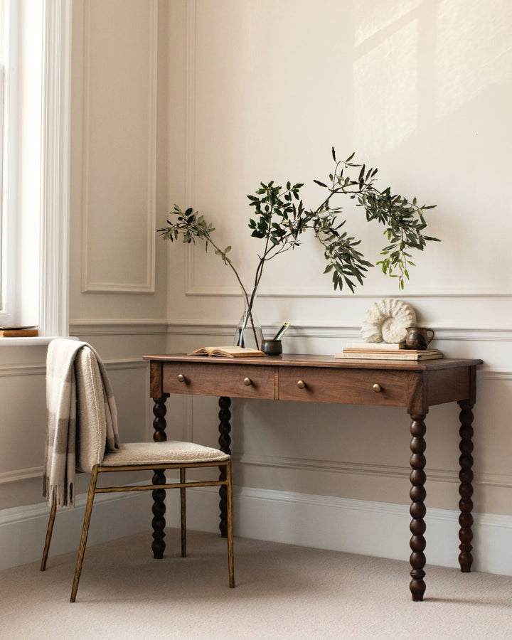 Wooden desk with chair and decorative items in a room with wainscoting.