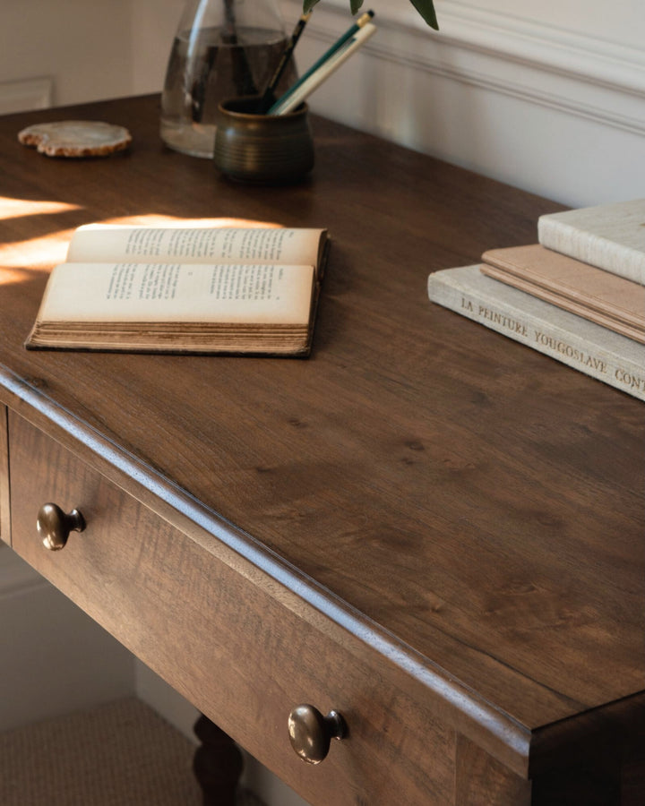 Wooden desk with open book, pen holder, and stacked books on a wooden surface.