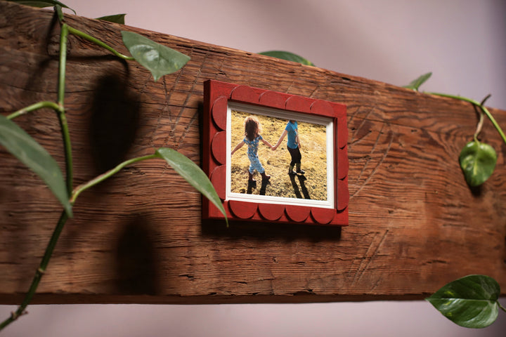 Red picture frame on a wooden surface with a photo of two children holding hands.