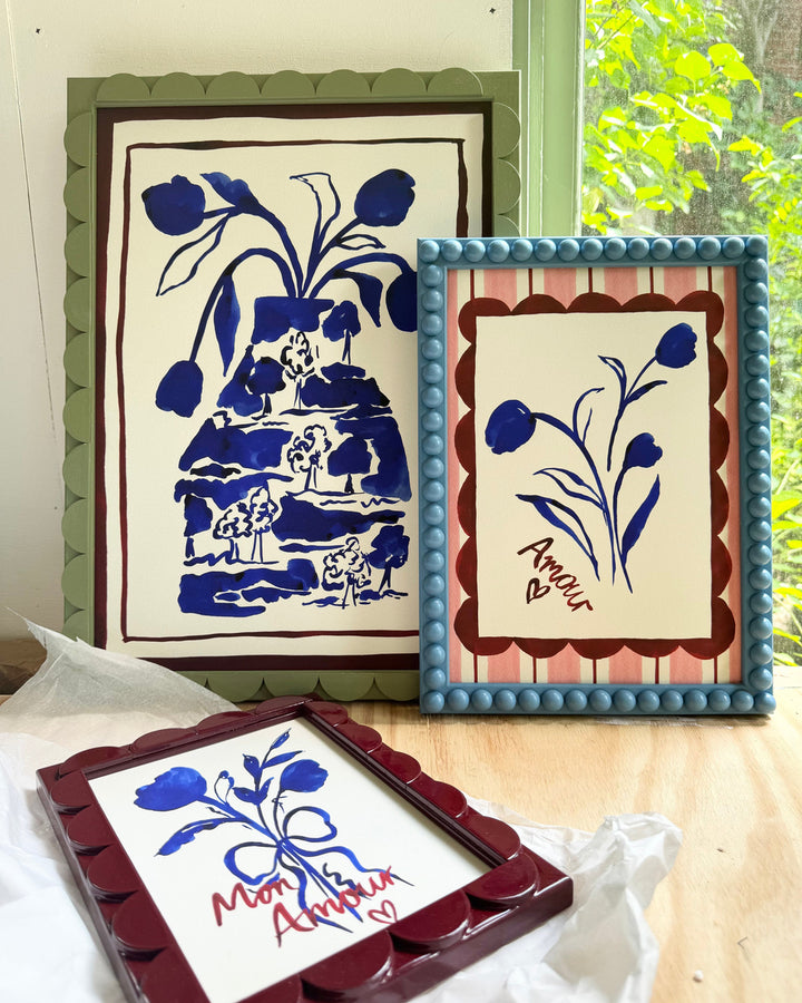 Three framed artworks with blue floral designs on a wooden surface.