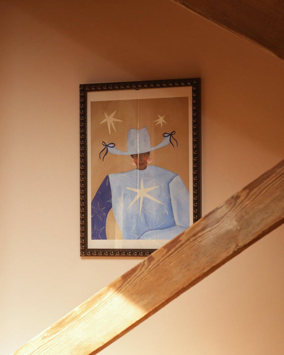 Framed artwork on a wall with wooden beams and sunlight filtering through.