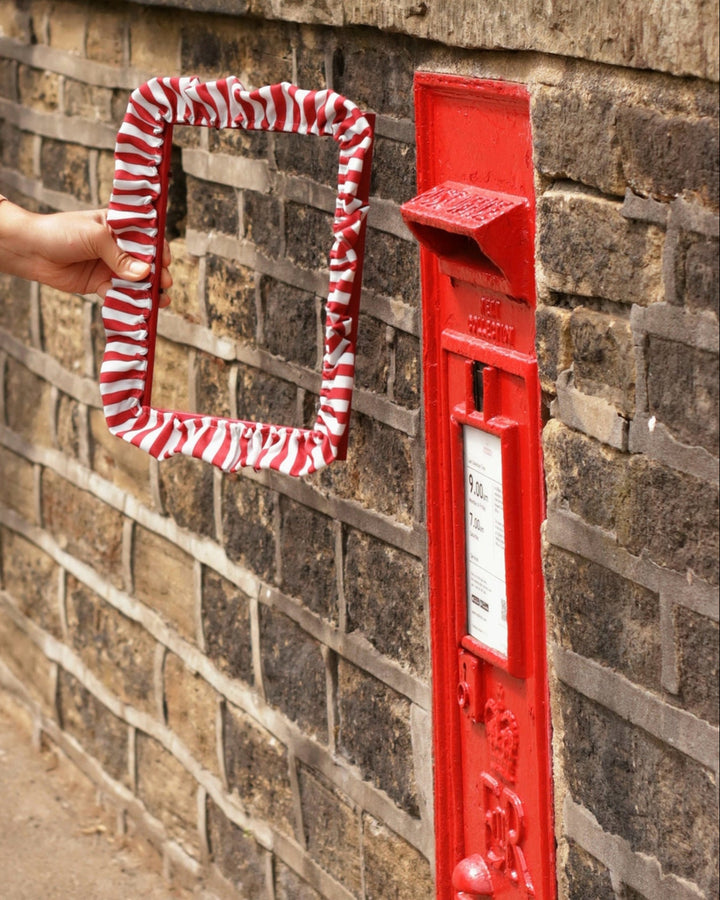 Red mailbox with a striped red and white cover attached to a brick wall.