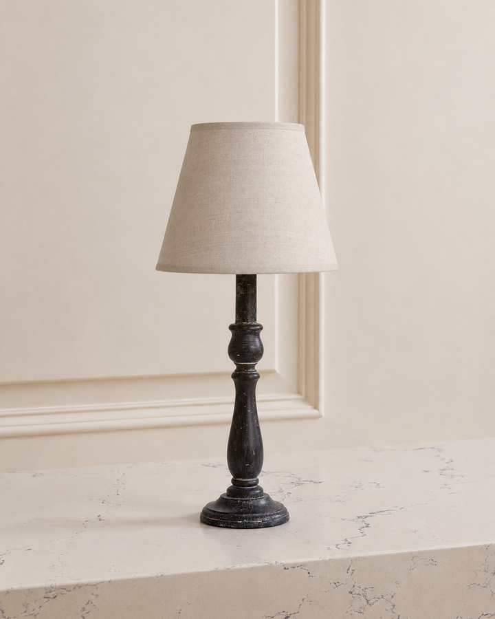 Table lamp with a beige shade on a marble surface against a neutral wall.