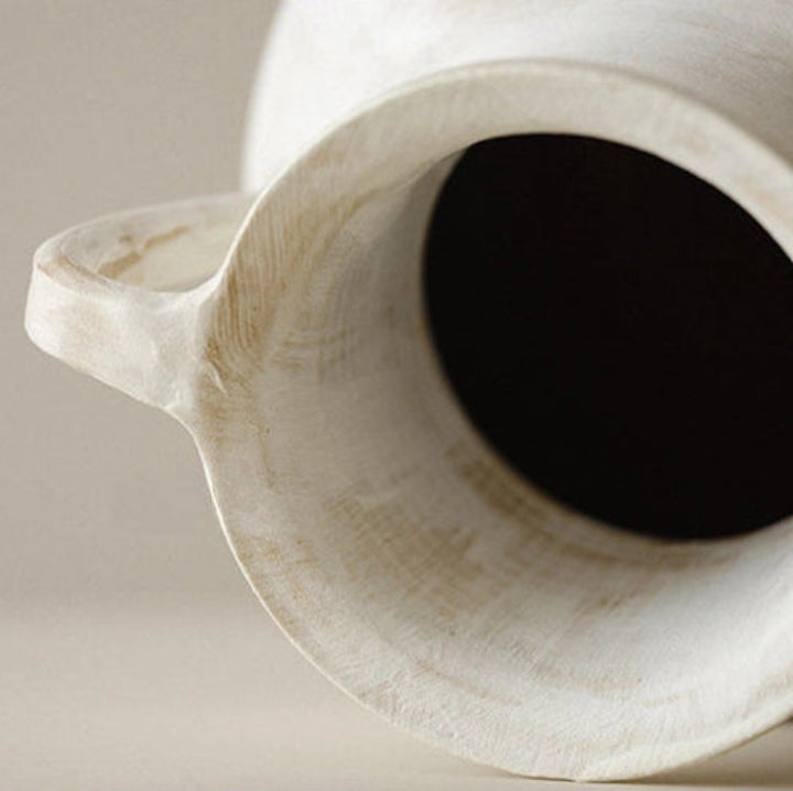Close up of a handmade cream ceramic vase, with a round shape, curved handle and a visible textured surface.
