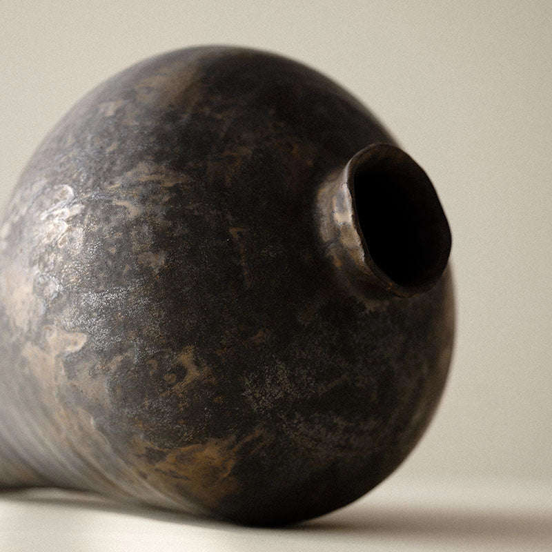 A handmade ceramic vase with a black and gold color scheme, with a round shape and a visible textured surface.
