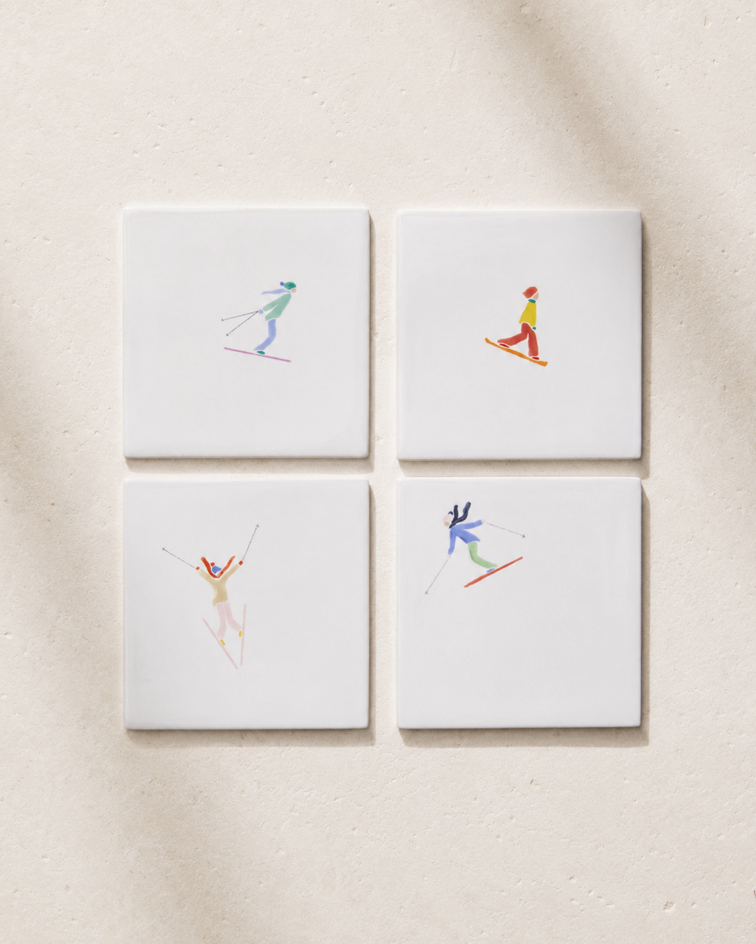 Four square coatsers with skiing illustrations on a beige background