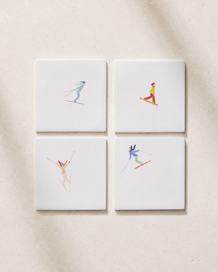 Four square coatsers with skiing illustrations on a beige background