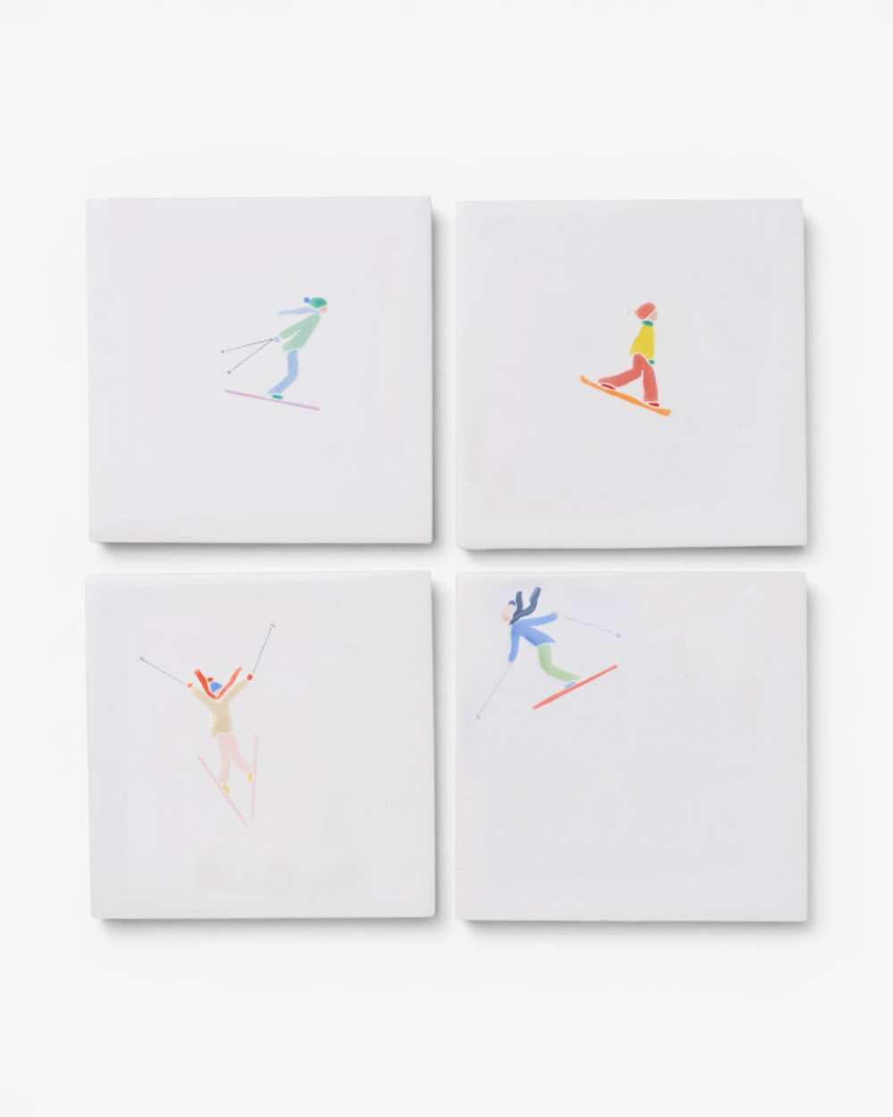 Four white ceramic coasters with colorful skier illustrations on a white background