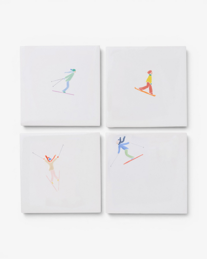 Four white ceramic coasters with colorful skier illustrations on a white background
