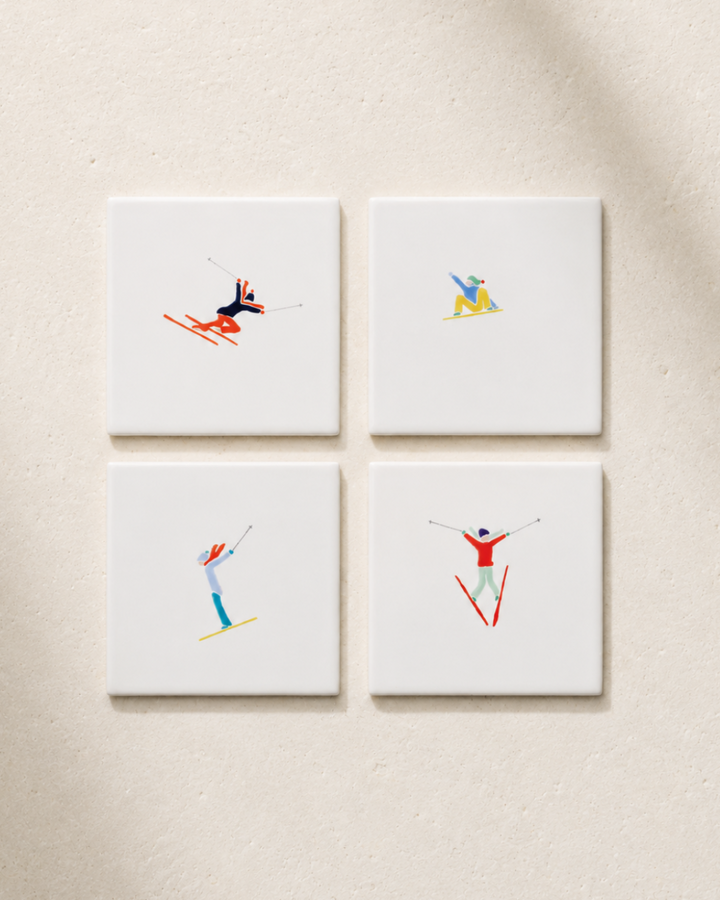Four coasters with skier illustrations on a beige surface
