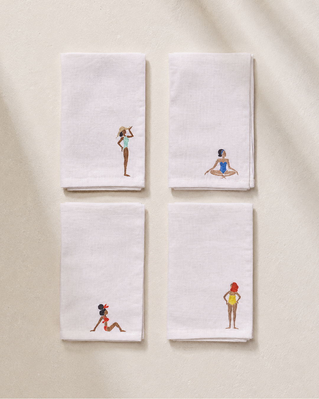 Set of four embroidered linen napkins with artistic designs on a beige background