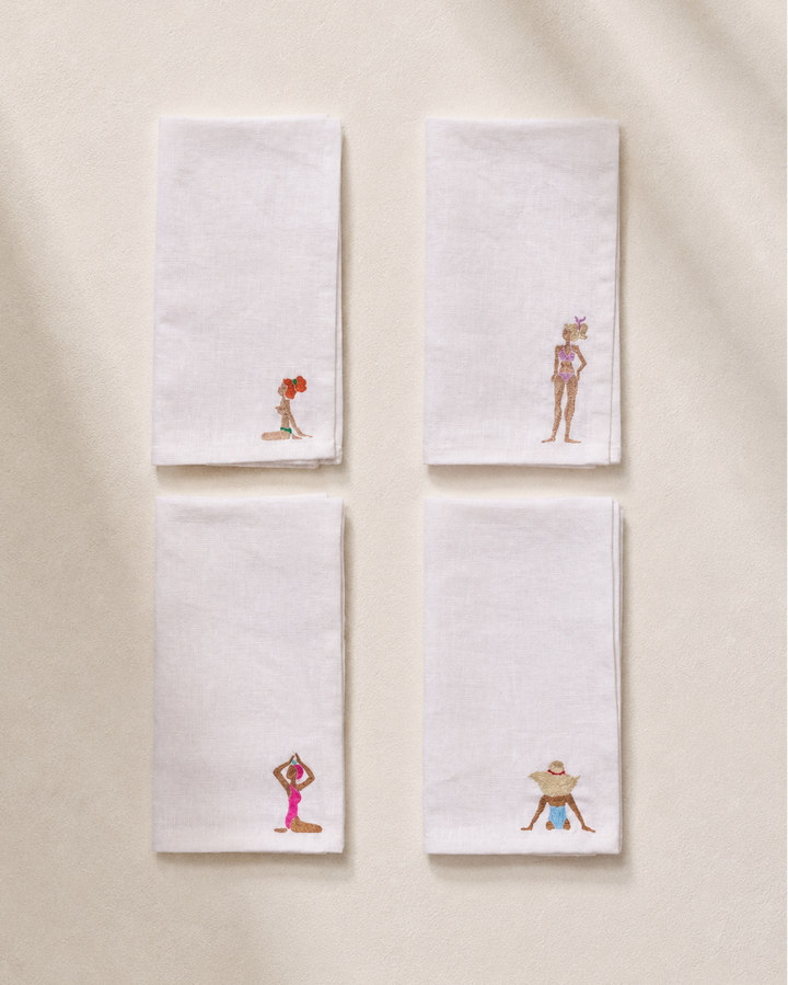 Four white napkins with embroidered designs of people in various poses on a beige background.