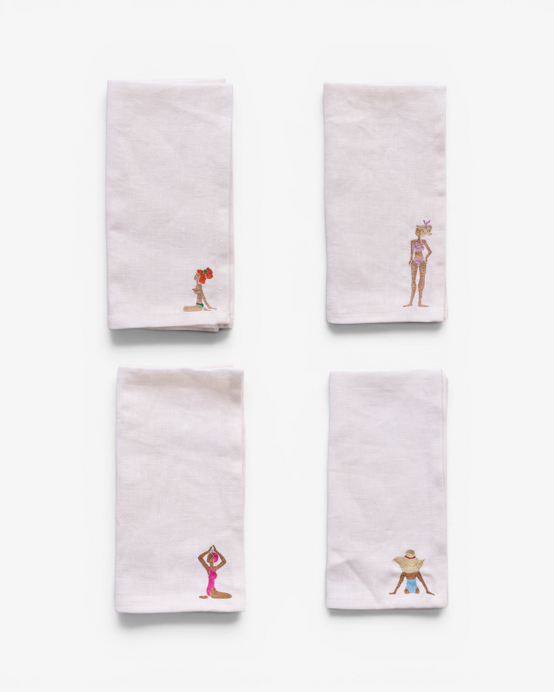 Four white napkins with embroidered designs on a white background